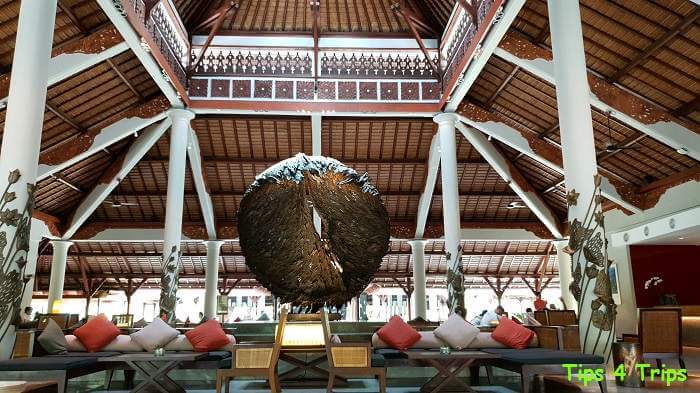 The Padma Legian lobby with thatched roof, large thatched hanging ball and couches with red and grey cushions