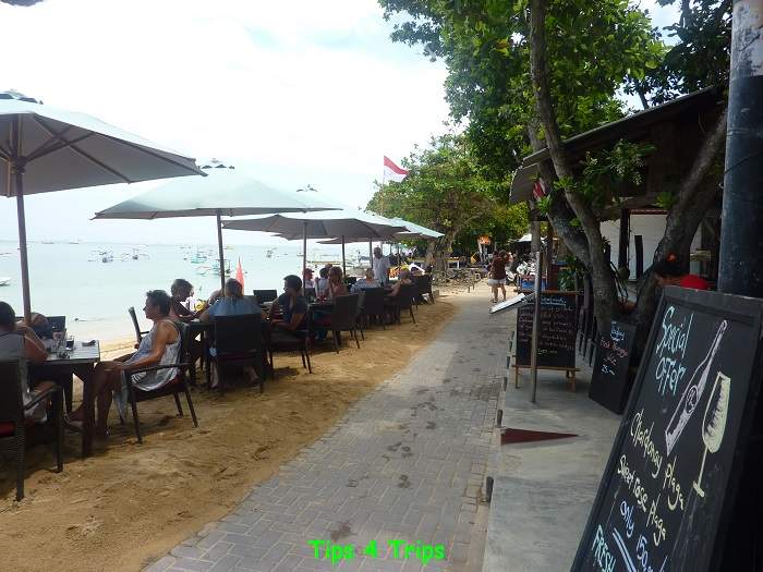 people sitting at restaurant tables along the beach in Bali during the day