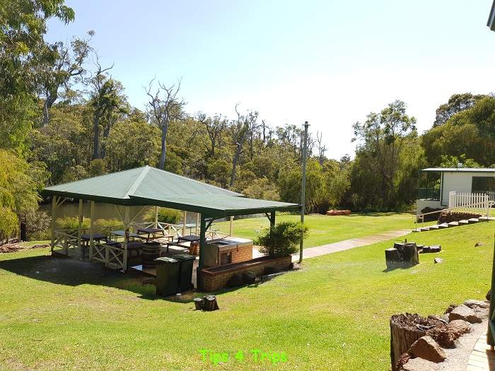 Large outdoor shaded area with BBQ and tables surrounded by grass 