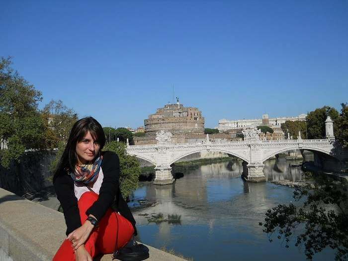 woman sitting on river wall in Rome with bridge, Castel Saint'Angelo and Vittoriano Monument in the background