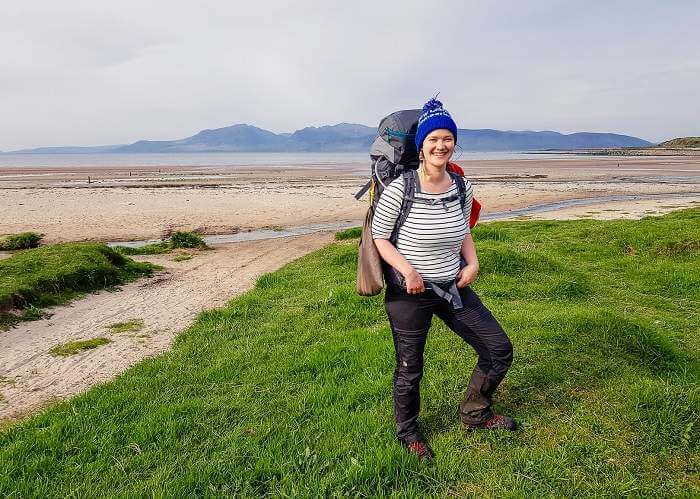 woman standing near mountainous lake wearing a trekking backpack