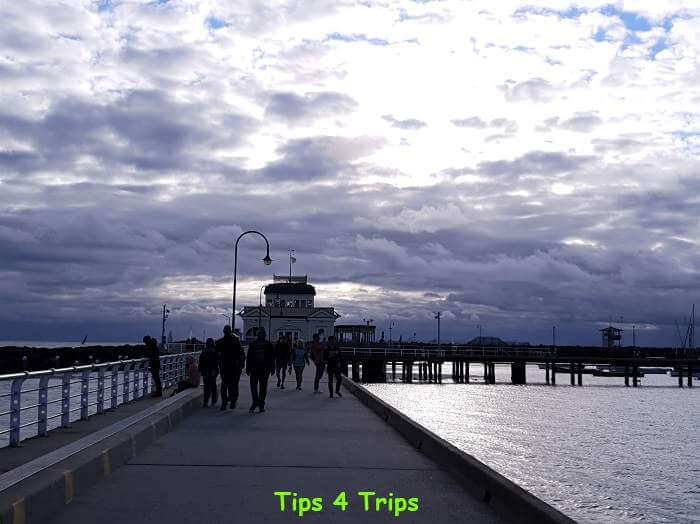 people walking along St Kilda pier with kiosk near the end of jetty