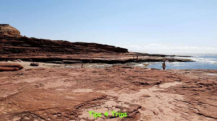 sheet of red rock jutting out to sea with people walking along them