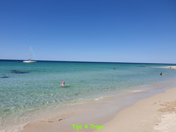 chils swimming in calm clear waters at Meelup beach in South Western Australia, sail boat in the background