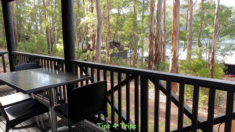 black plastic chairs and timber railed balcony looking through forest trees to lake